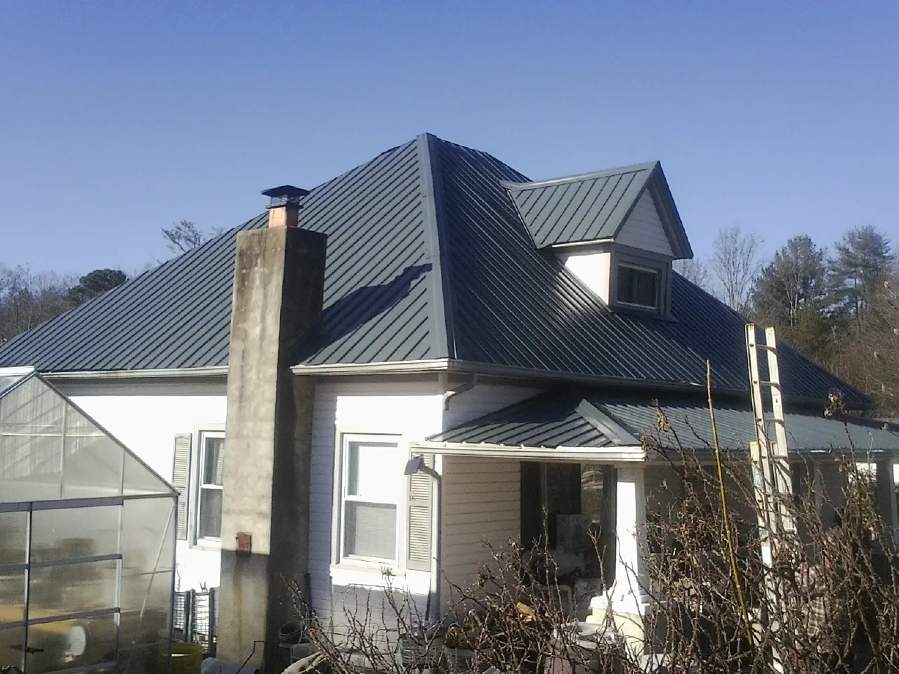 Dark blue standing seam metal roof on a white farmhouse with dormer — Slate & Tile Roof Repair by Roofing Brothers in Mitchells