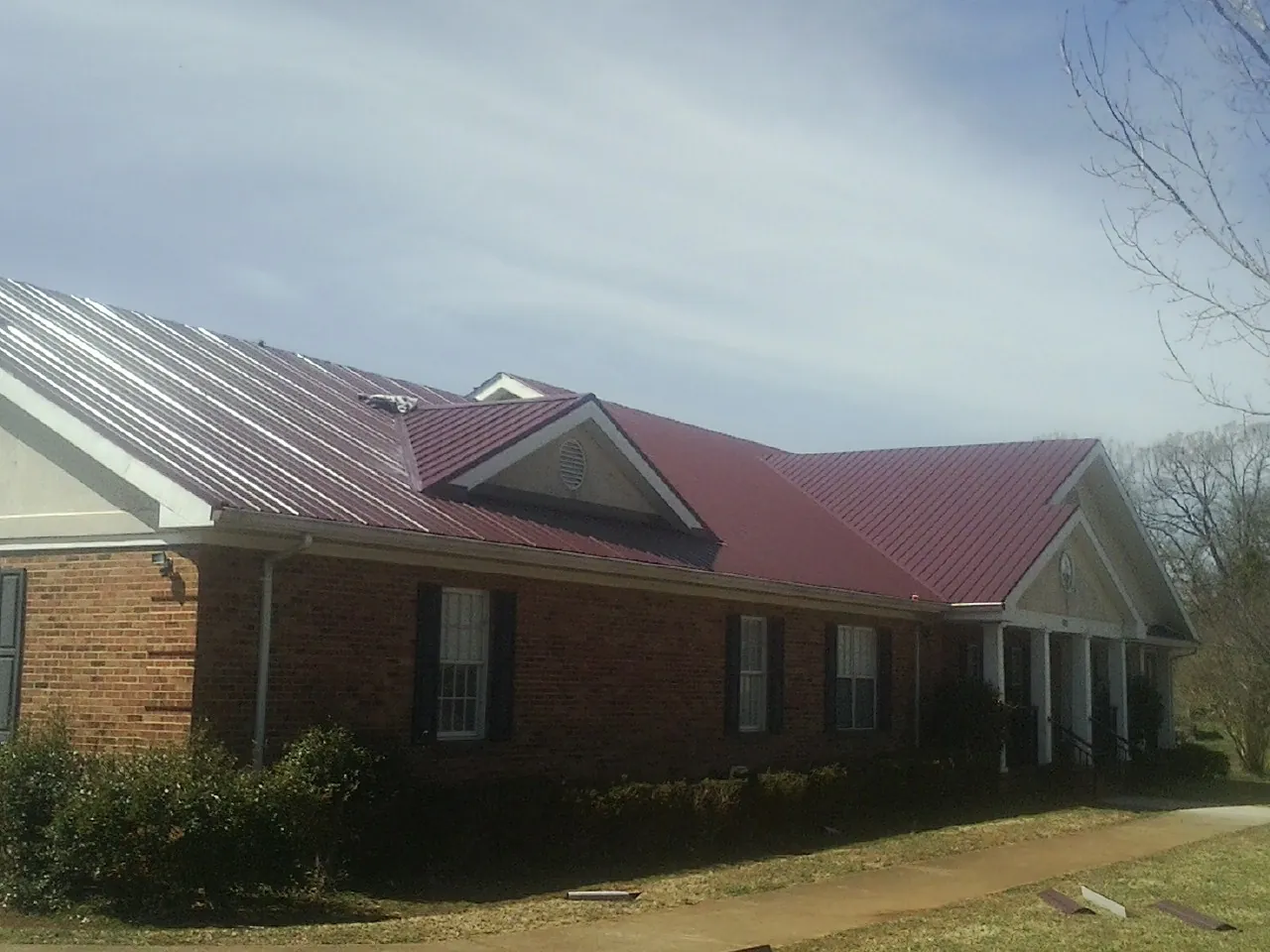 Red metal roof with gabled entries on a long brick building, from a Hail Damage Roof Repair job in Mitchells