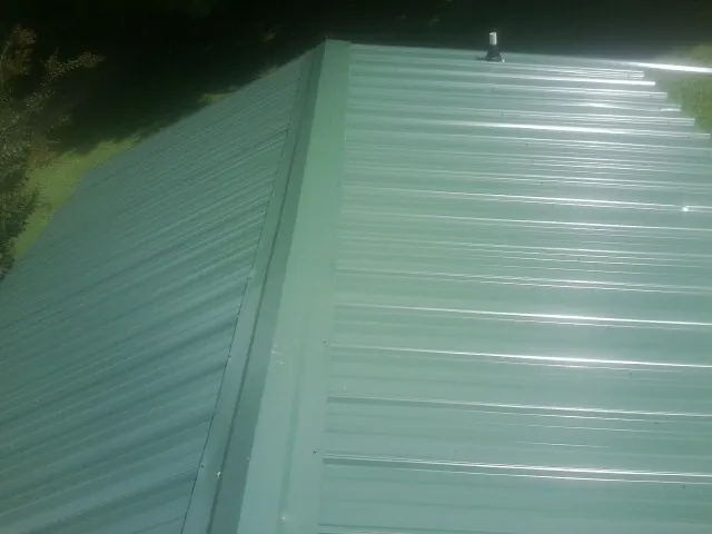 New green metal panels meeting at the ridge of a roof — Flat Roof Repair work by our crew in Mitchells