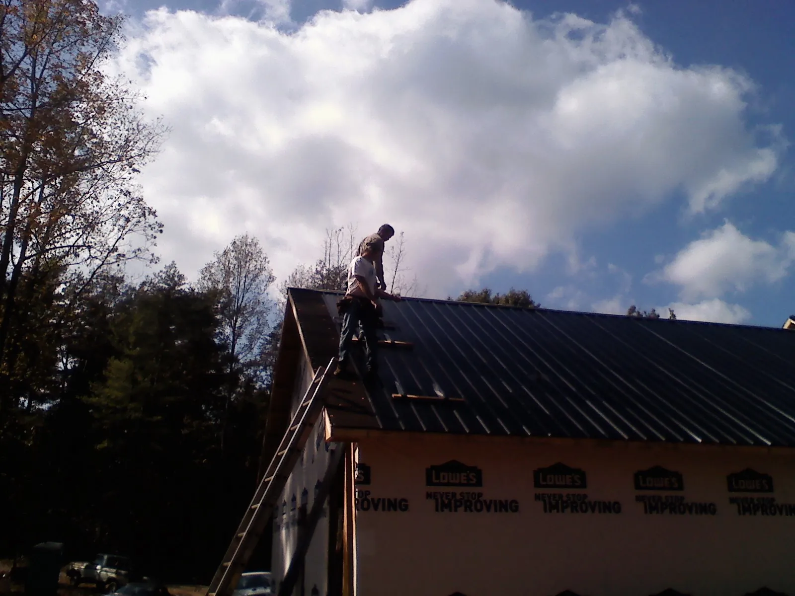 Roofer fastening dark metal panels high against a cloudy sky, from a Roof Inspection job in Mitchells