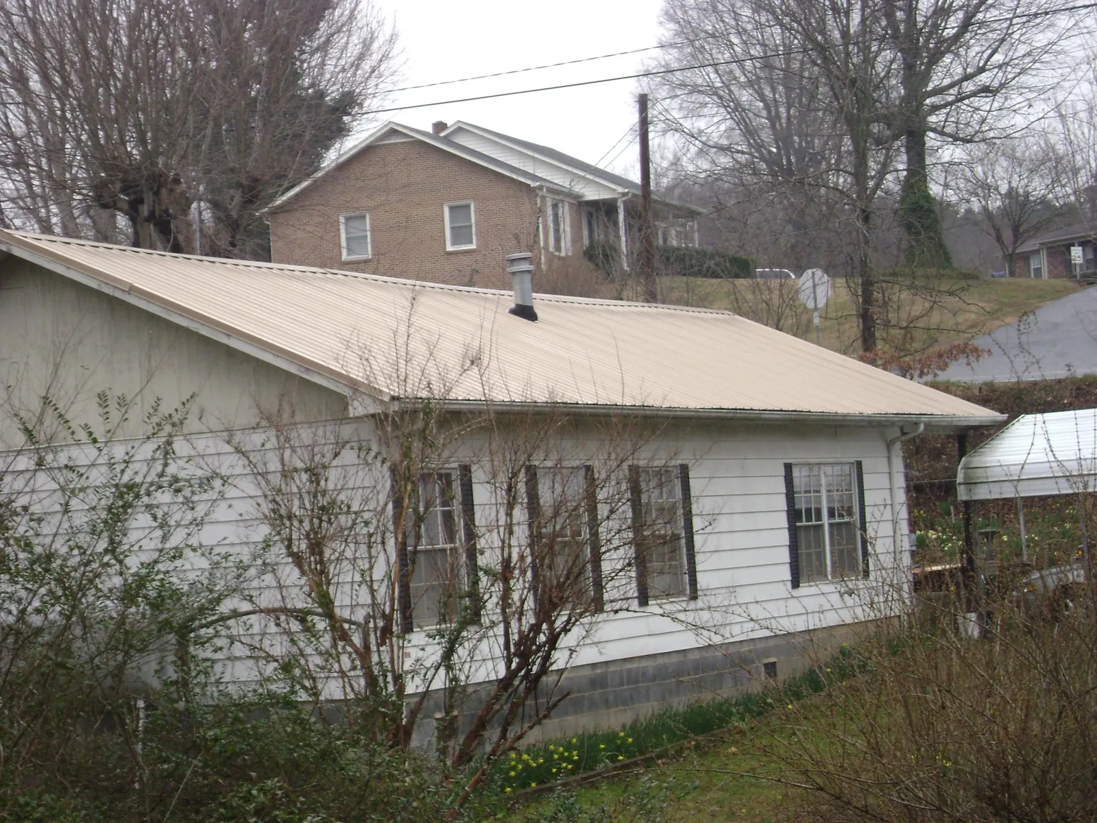 Tan metal roof on a white sided house set into a hillside — Commercial Roofing by Roofing Brothers in Mitchells