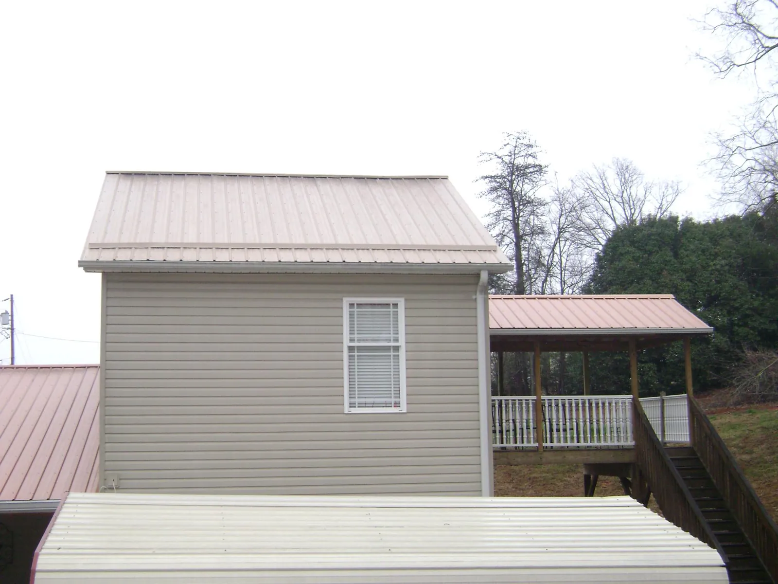 Tan metal roofs on a two story addition and attached porch, from a Roof Replacement job in Mitchells